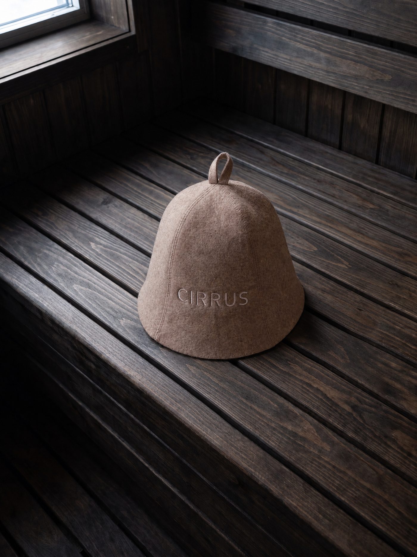 Moorit wool sauna beanie resting on a dark aspen sauna bench in window light
