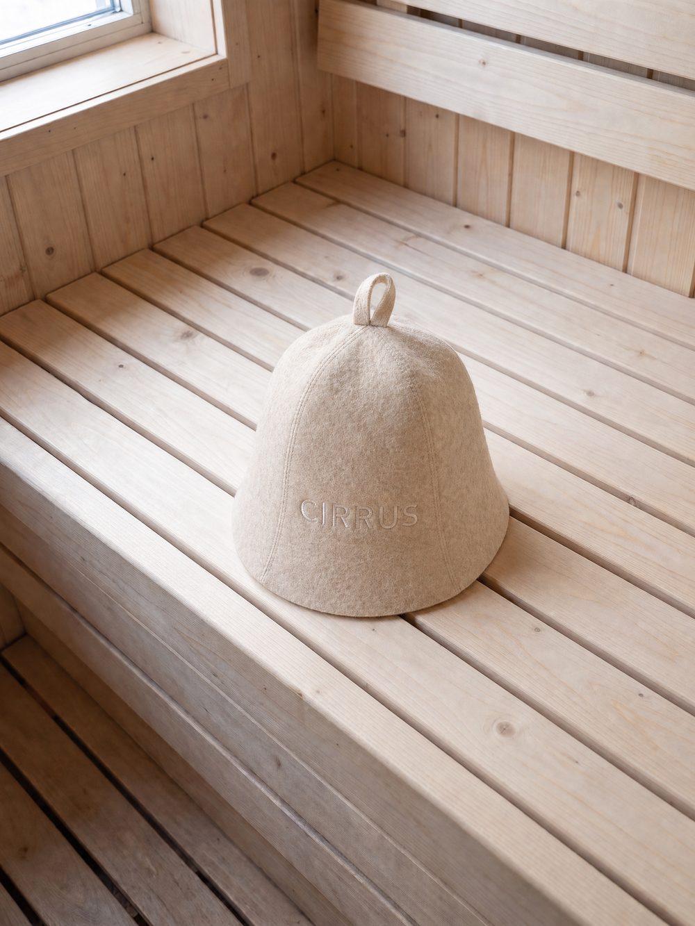 Light beige wool sauna beanie on a pine bench